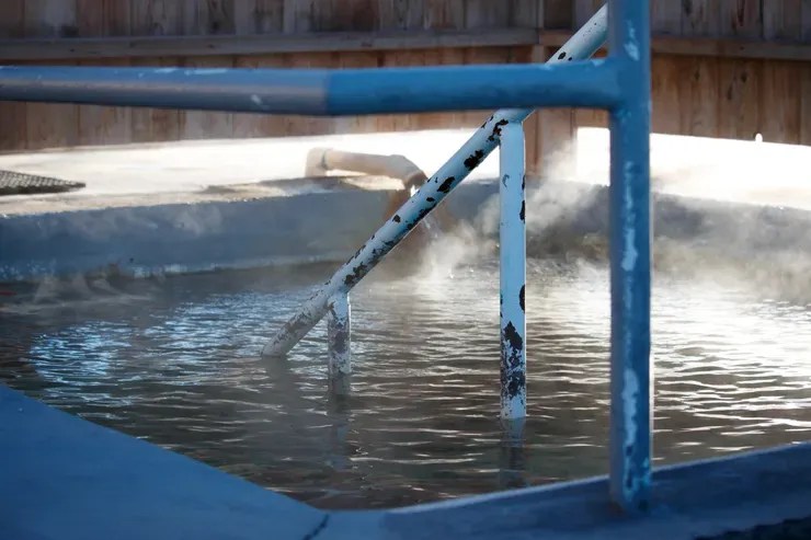 Outdoor hot spring with metal railing and steam rising from water.