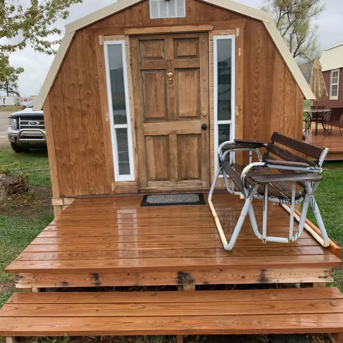 Wooden shed with porch, two chairs, and a door with windows.