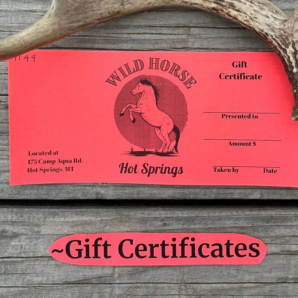 Red gift certificate on wooden surface with antler beside it.