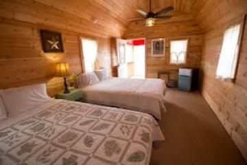 Wood-paneled room with two beds, a lamp, paintings, and a ceiling fan.