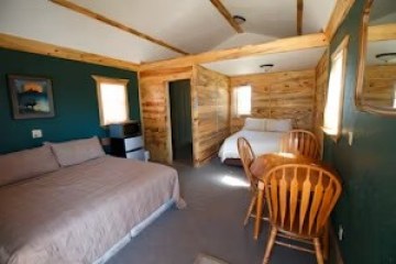 Cozy cabin interior with two beds, a small table, and wooden walls.