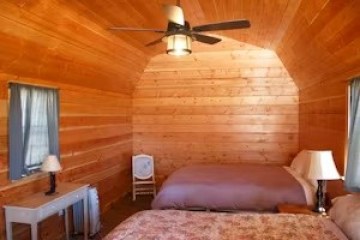Wood-paneled room with two beds, ceiling fan, lamps, and small desk.
