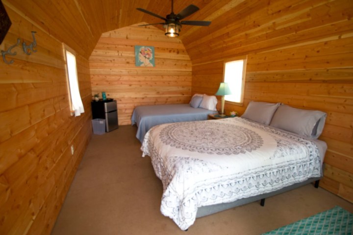 Wood-paneled bedroom with two beds, a fan, and a small fridge.