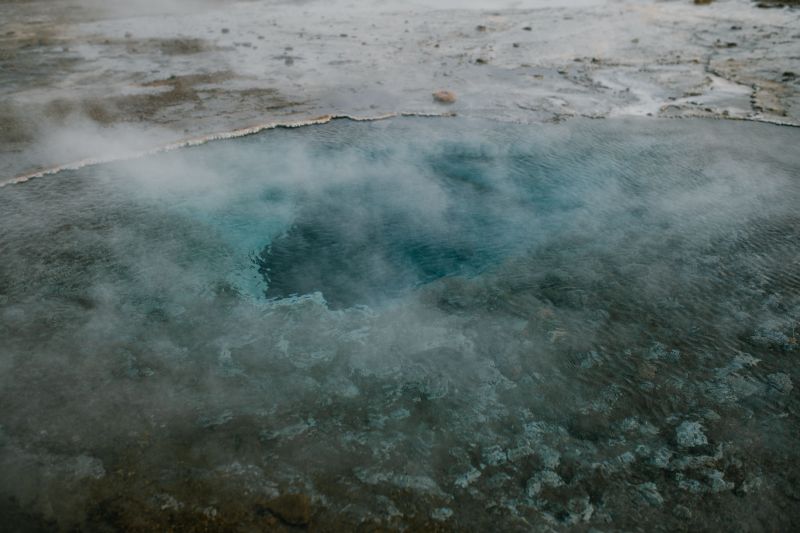 Geothermal hot spring with steam rising from blue water.