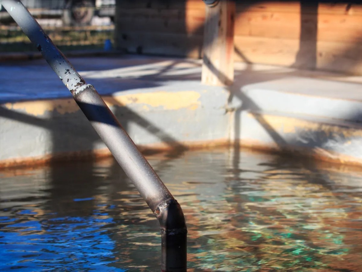 Metal handrail next to a small outdoor pool with wooden walls.