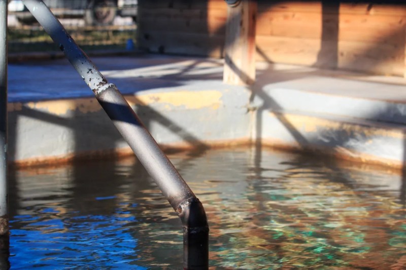 Metal handrail next to a small outdoor pool with wooden walls.