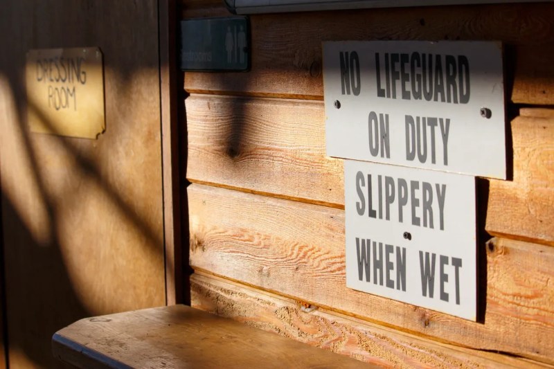 Wooden wall with signs: 'No Lifeguard on Duty' and 'Slippery When Wet'.