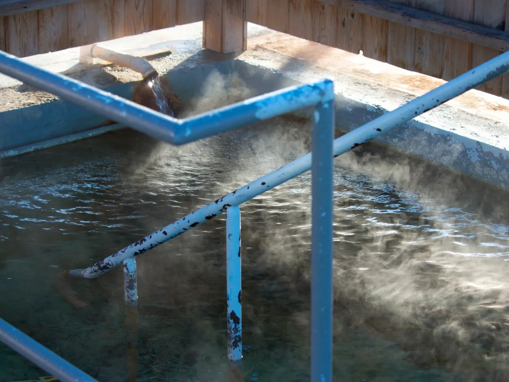 Steam rising from a hot spring with metal rails and wooden structure.
