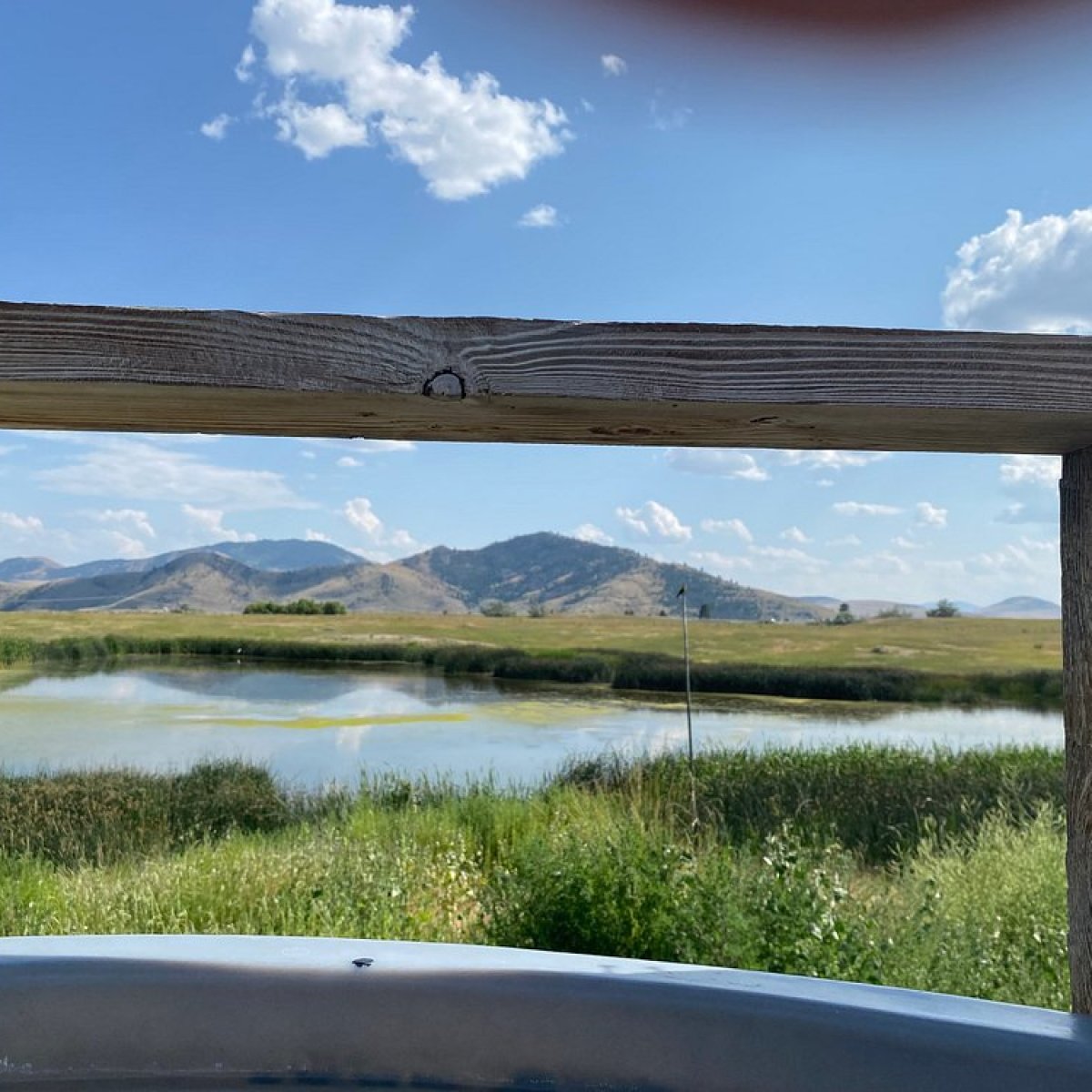 Scenic view of hills and a lake through a wooden frame on a sunny day.
