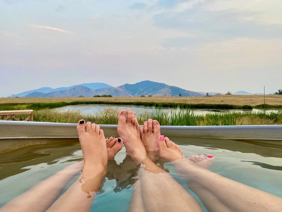 Three pairs of feet in a hot tub facing a scenic mountain view.