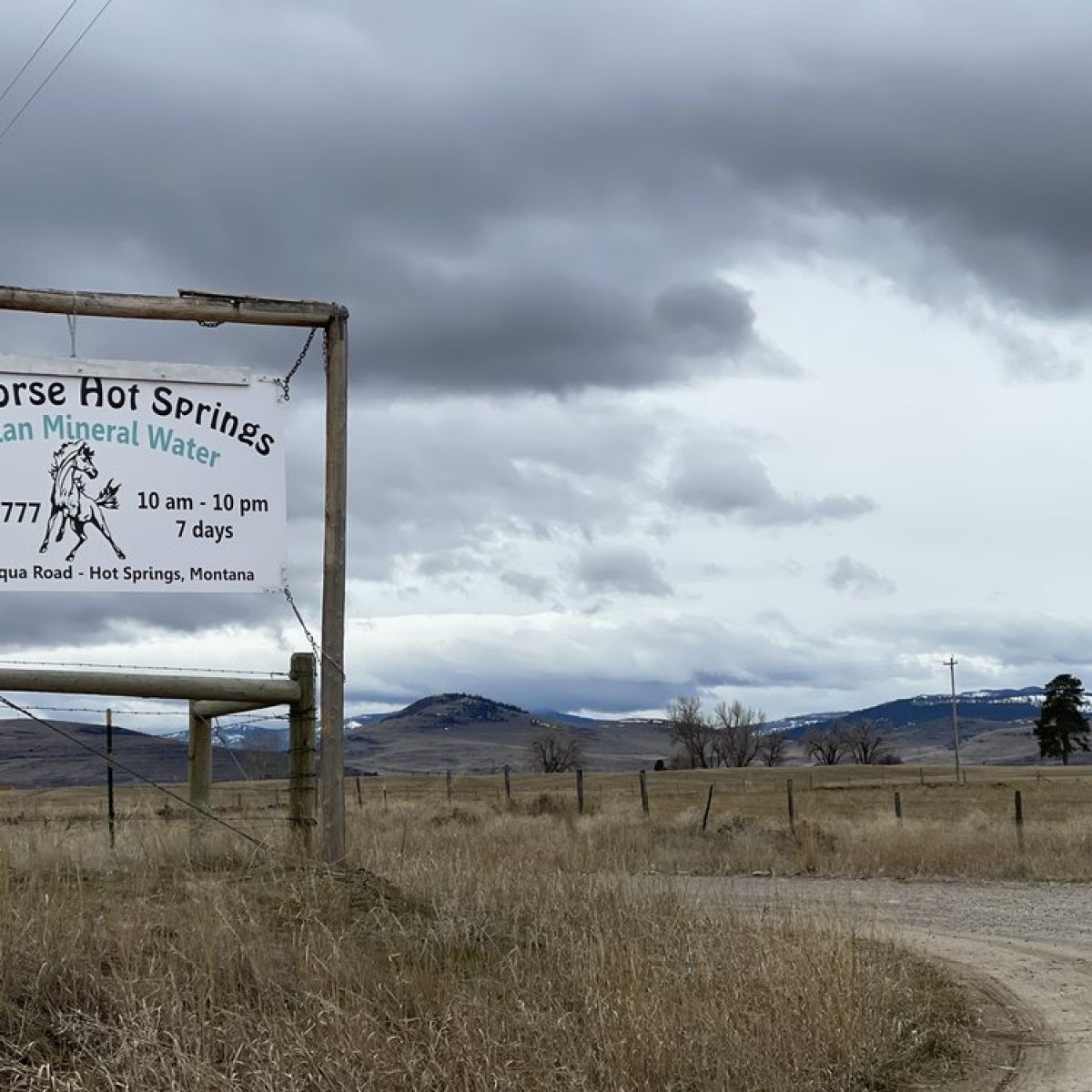 Sign for Wild Horse Hot Springs with cloudy sky and rural landscape.
