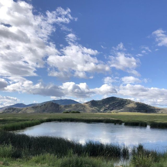 Scenic view of pond and mountains with a bench and tub in the foreground.
