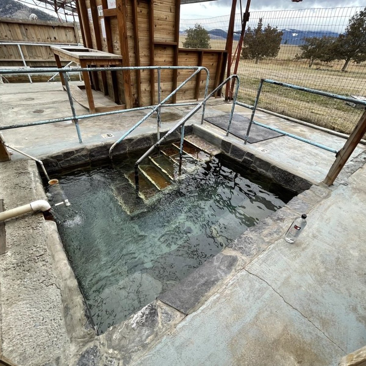 Outdoor hot spring with stone steps and wooden railing.